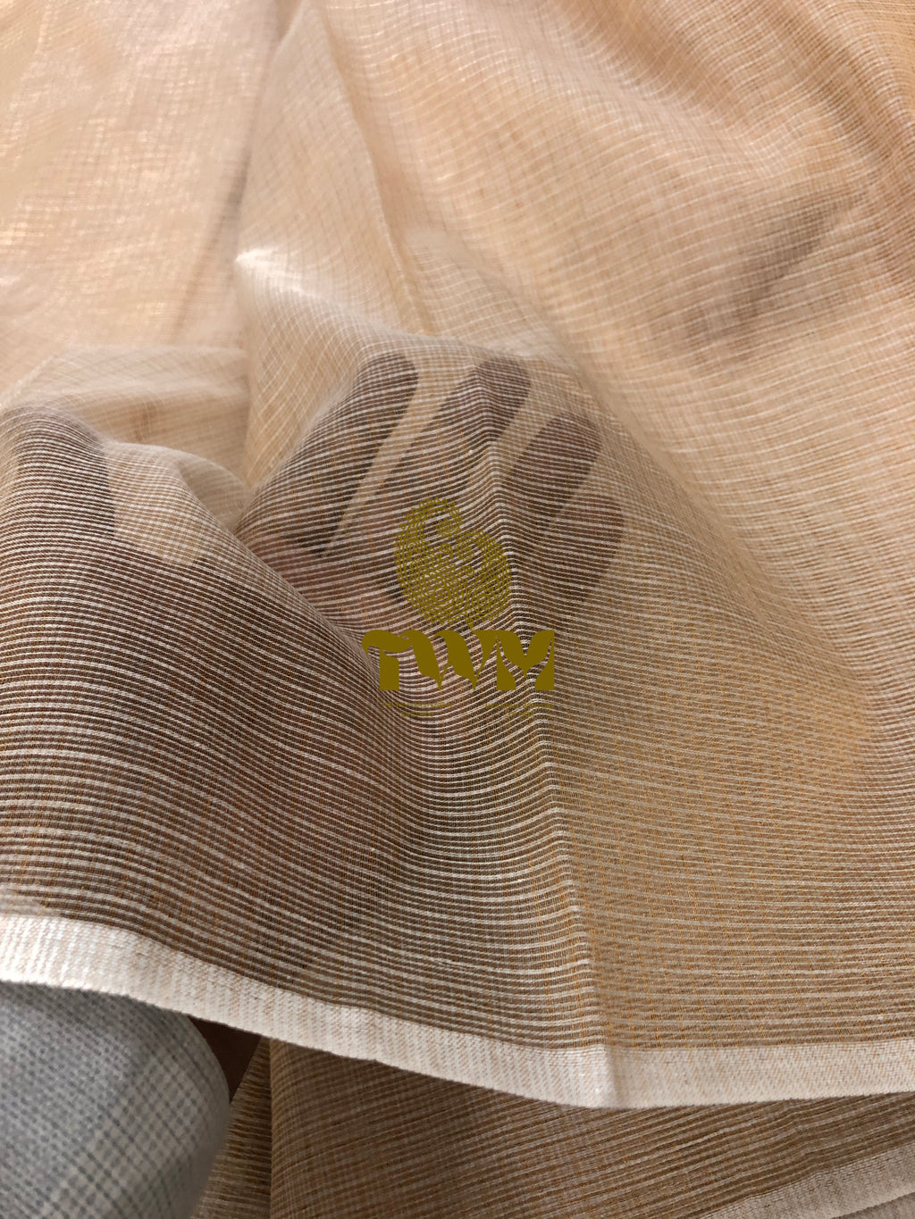 Close-up of beige fabric with a logo, possibly The Weavers Museum, on a light background.