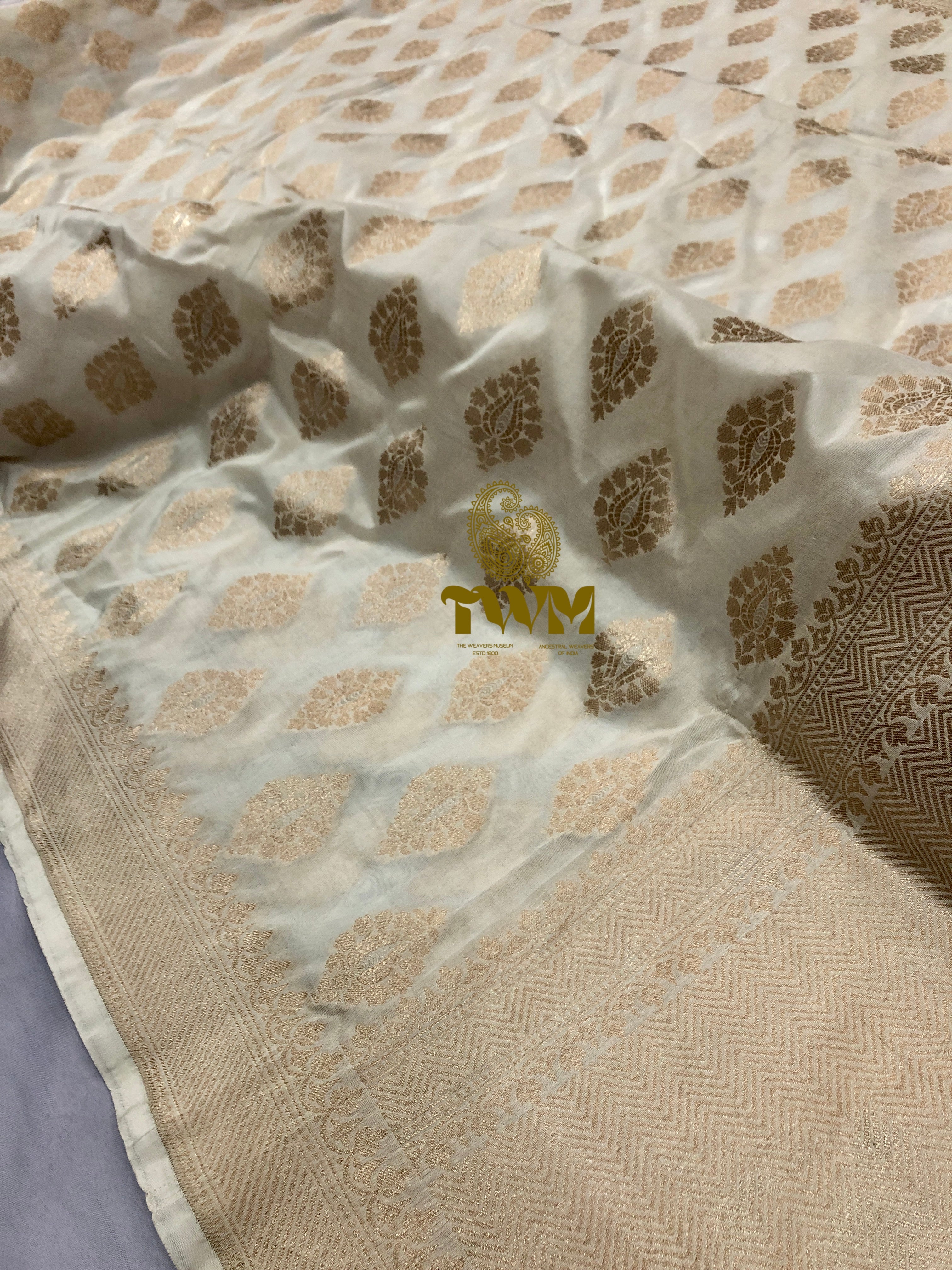 Beige fabric with gold leaf pattern and 'TM' logo on a gray background