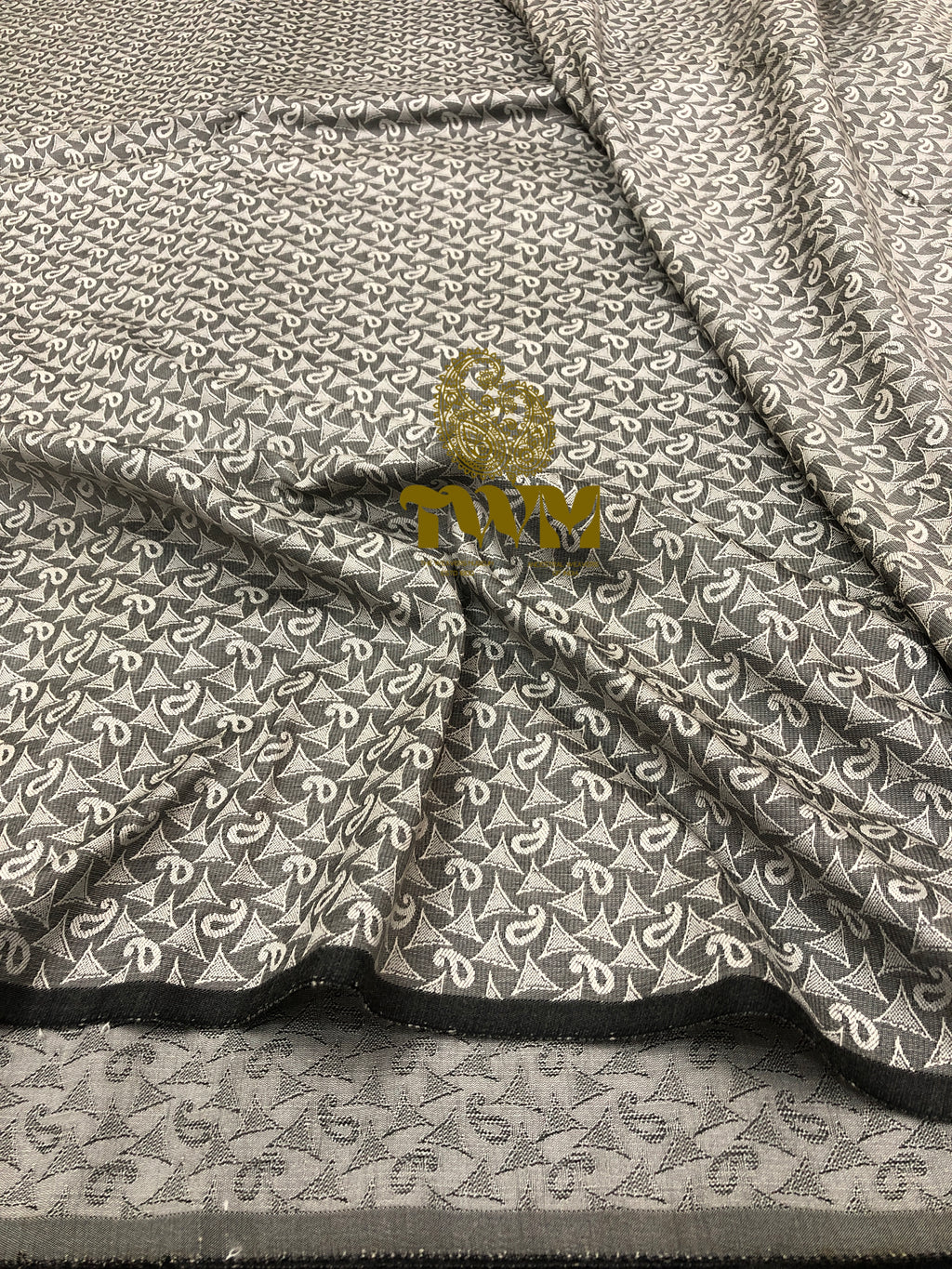 Textile with a geometric pattern and a gold emblem on a gray background