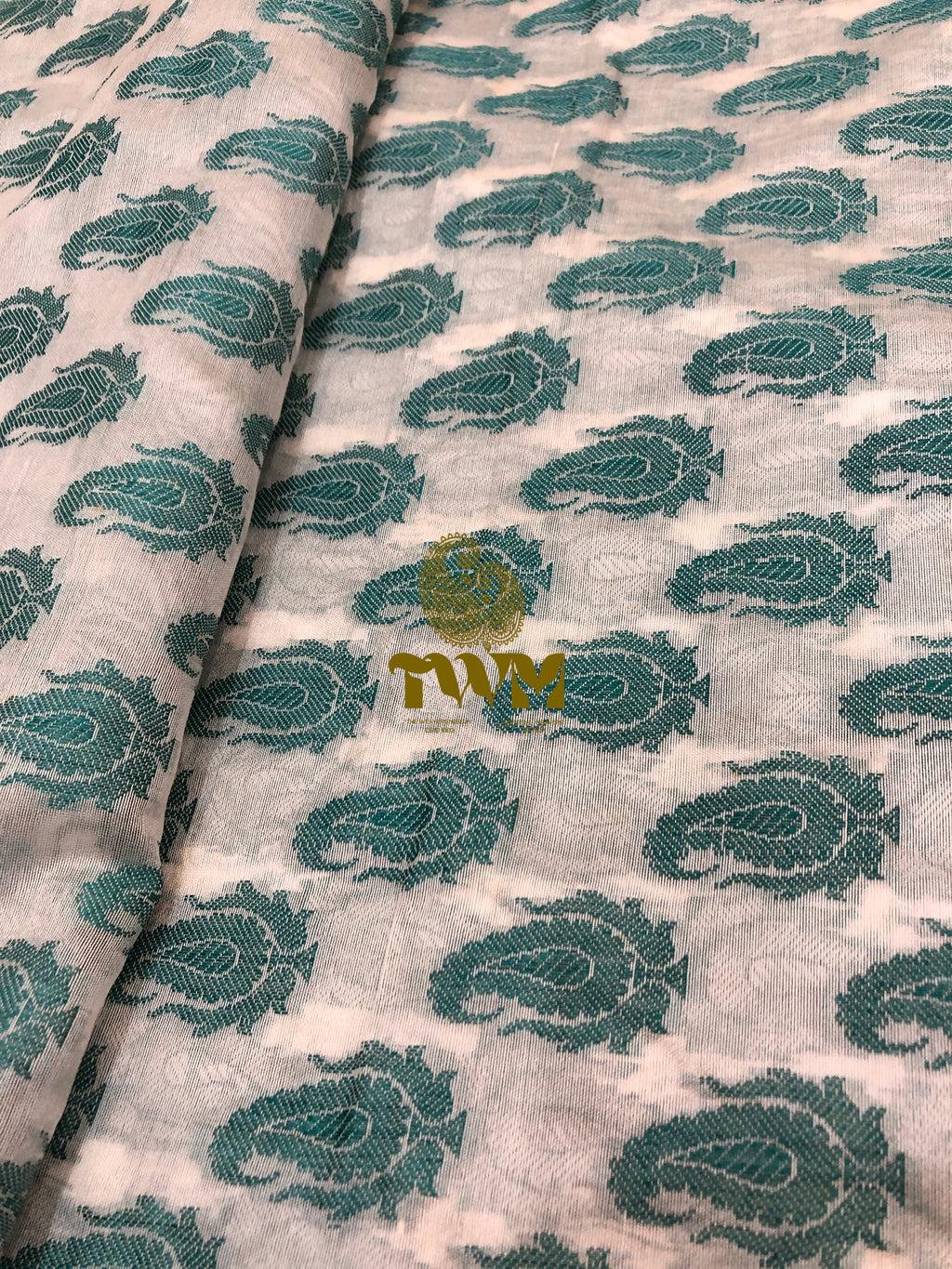 Fabric with green paisley pattern on a white background, featuring a visible brand logo.