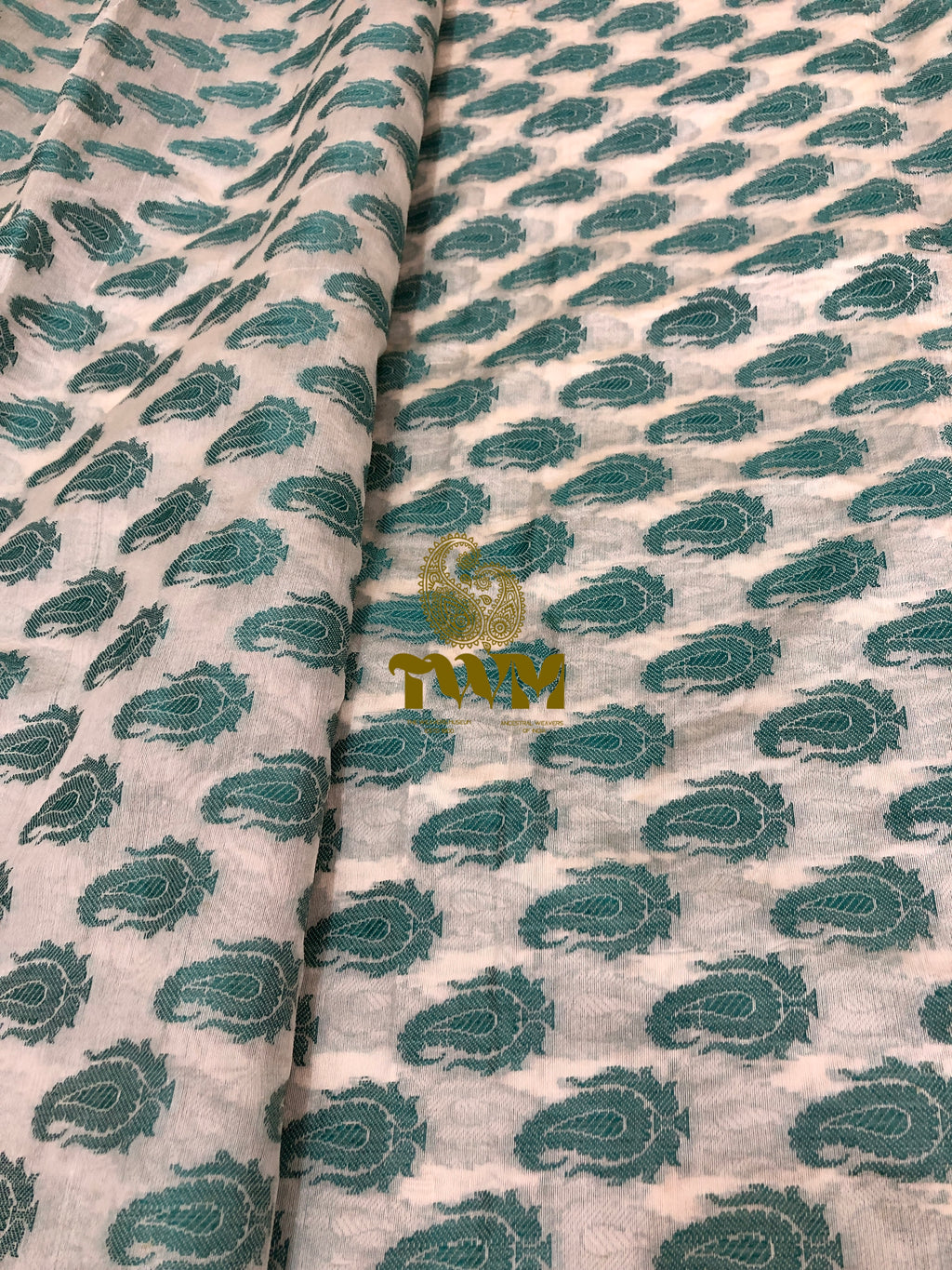 Fabric with green paisley pattern and a visible brand logo on a light background