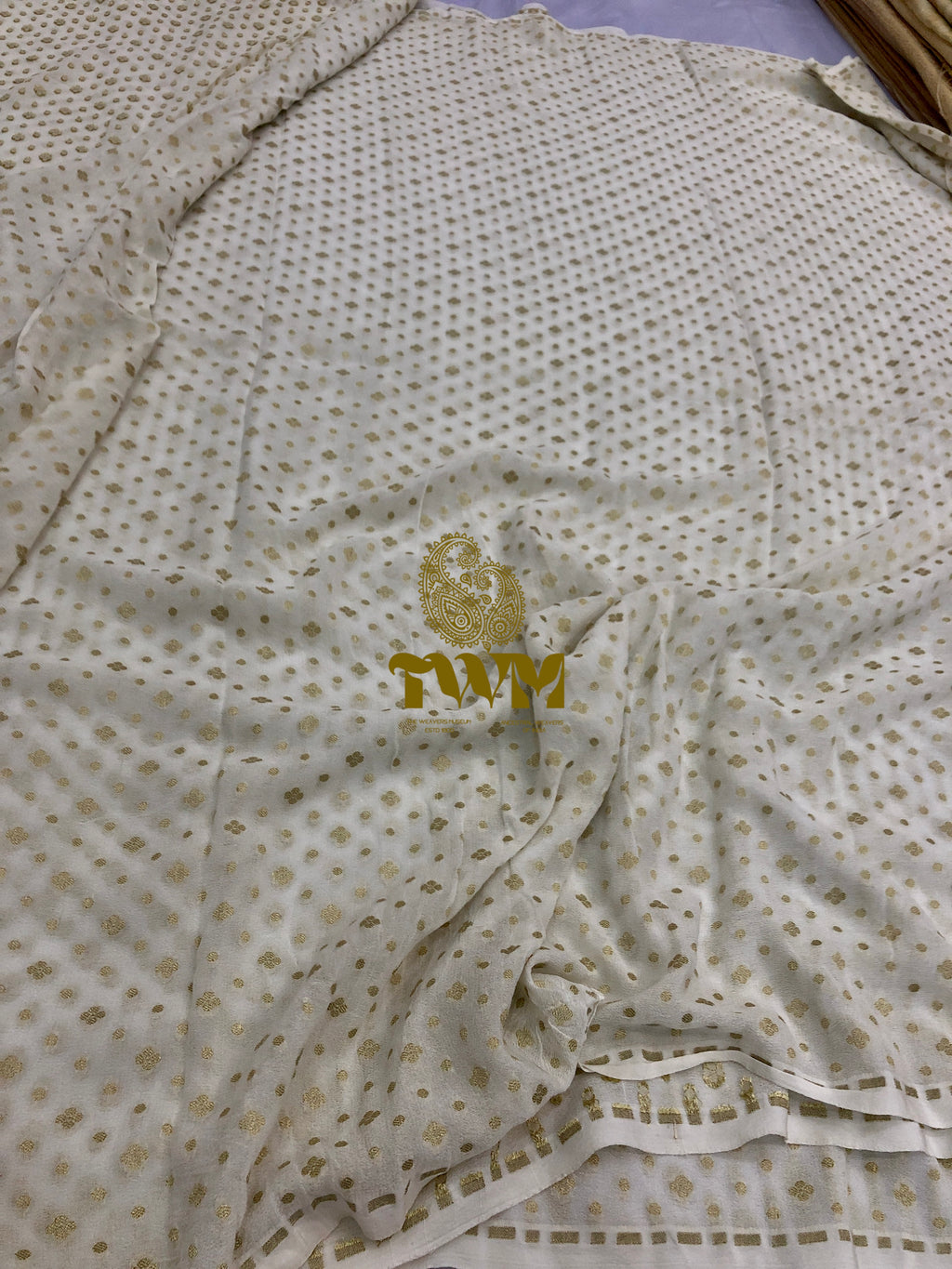 Folded fabric with gold patterns and 'TWM' logo on a light background