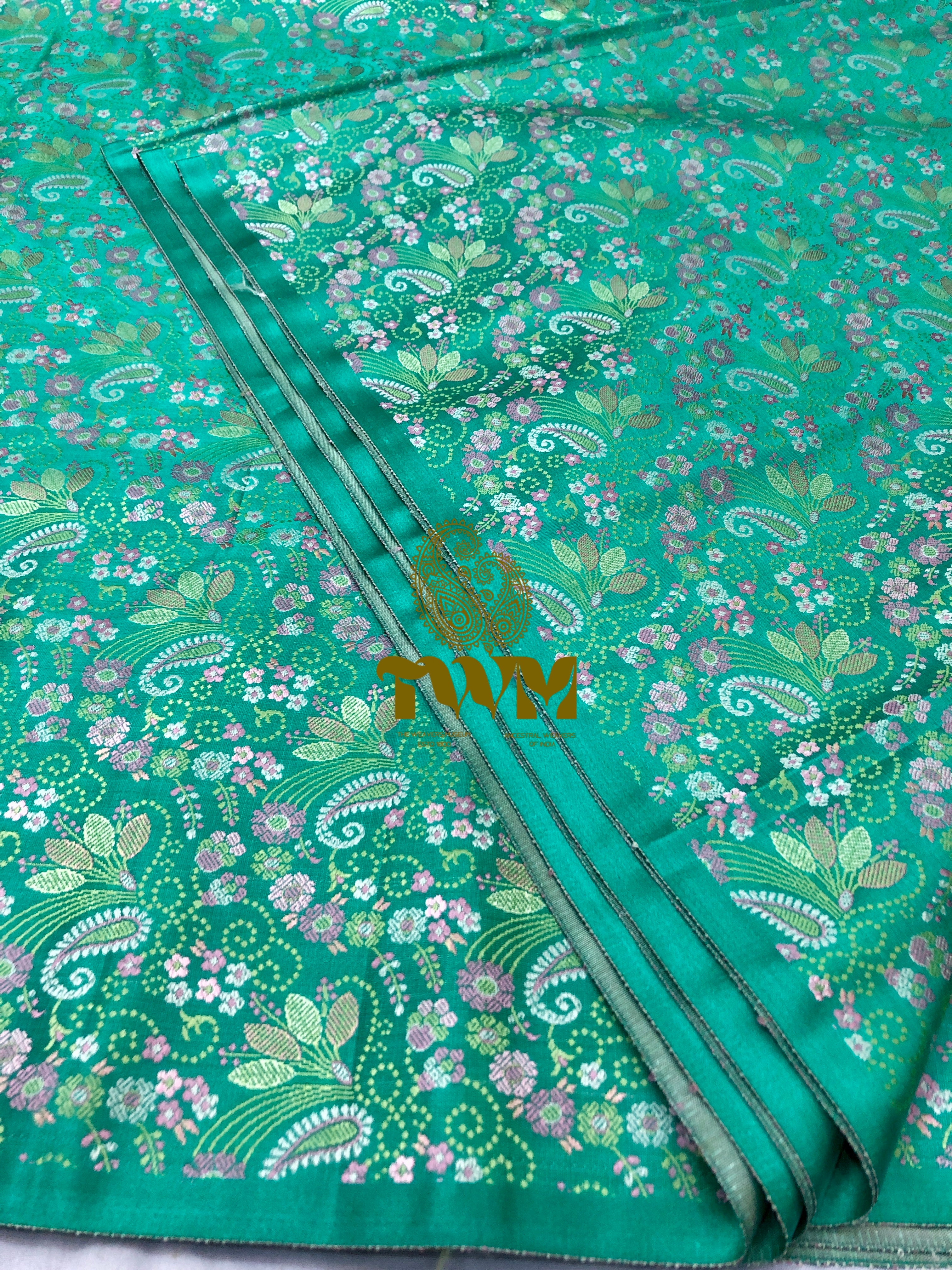 Green fabric with floral and paisley patterns, featuring a brand logo.